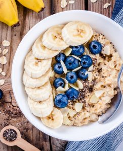 overnight oatmeal in white bowl topped with banana and blueberries with spoon in bowl