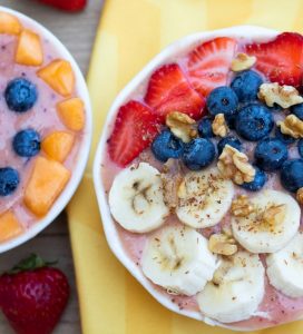 fruit smothie bowls in white glass bowls topped with blueberries, banana, strawberries, and walnuts