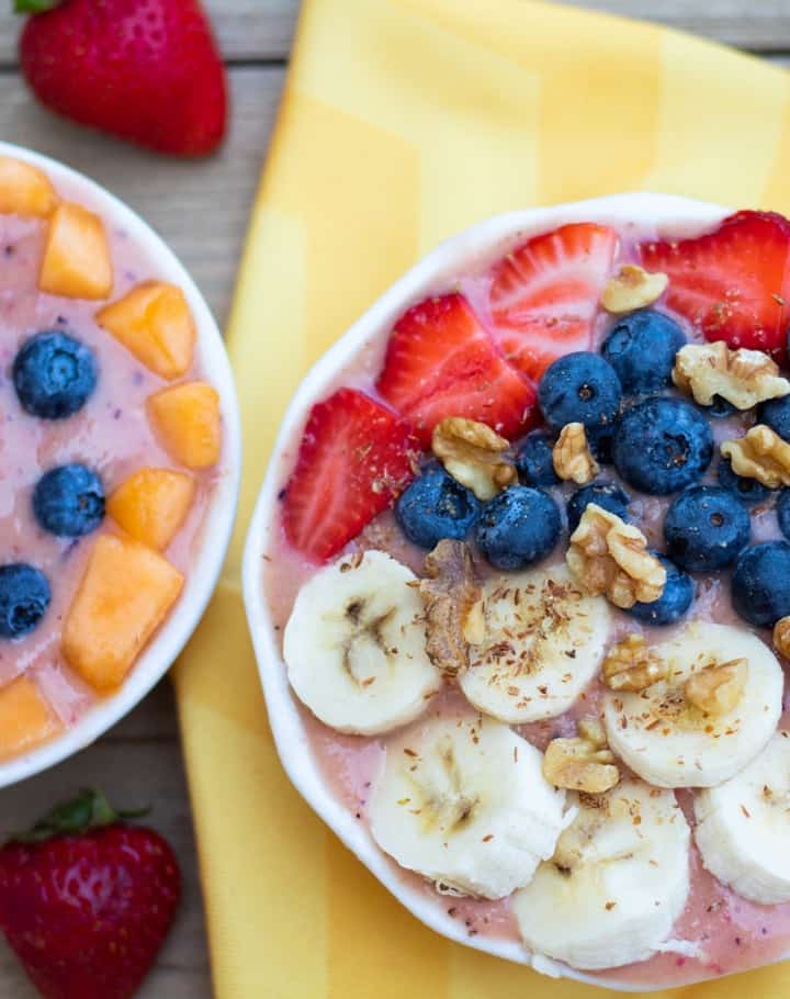 fruit smothie bowls in white glass bowls topped with blueberries, banana, strawberries, and walnuts
