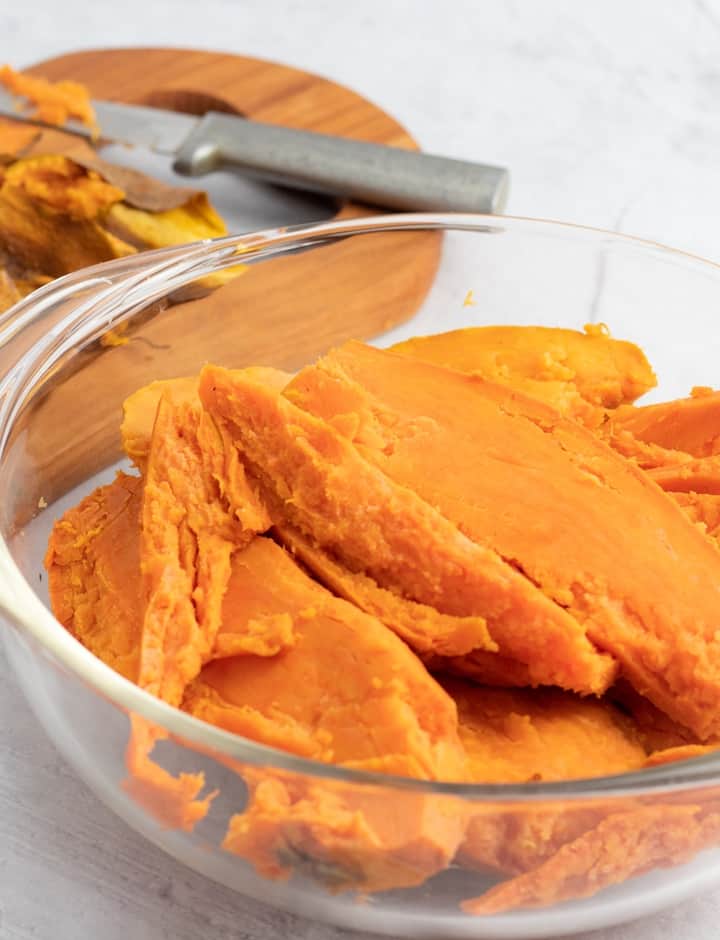 peeled sweet potatos in glass bowl with cutting board in background