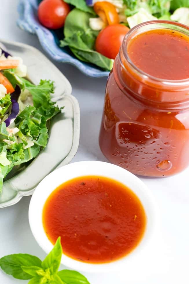 vegan oil free tomato salad dressing in dish and mason jar sitting beside salad
