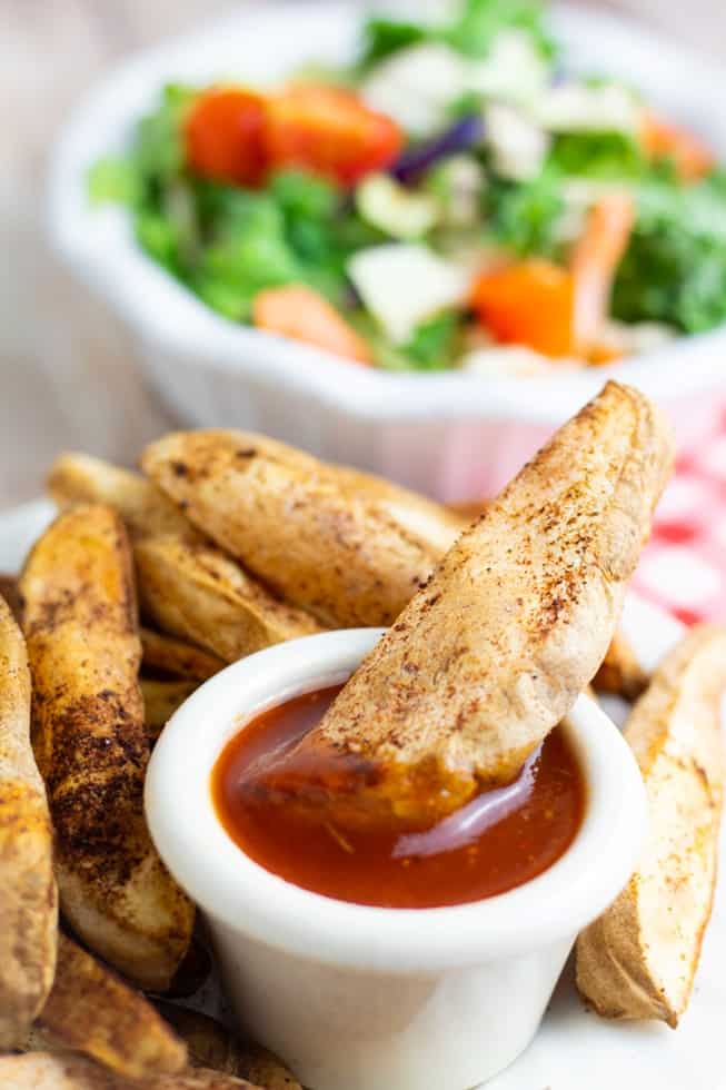 french fry dipped into a white dish with oil free salad dressing and salad in background