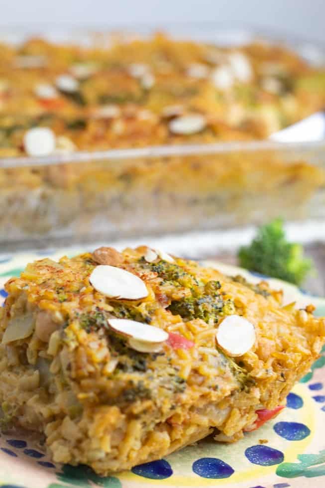 slice of vegan broccoli casserole on colorful plate with whole casserole dish in background