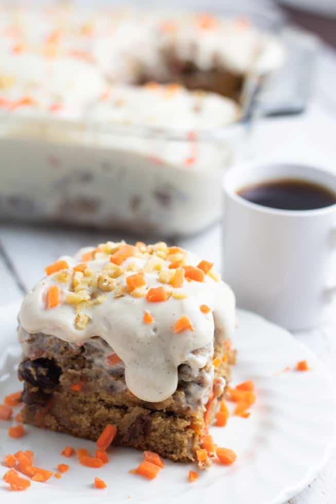 slice of carrot cake with white icing dripping off and white cup of coffee in background
