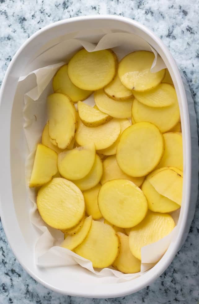 white casserole dish with sliced potatoes on parchment paper