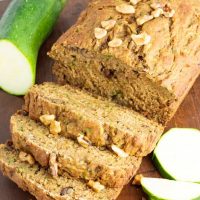 close up of sliced vegan zucchini bread on wooden board with zucchini beside