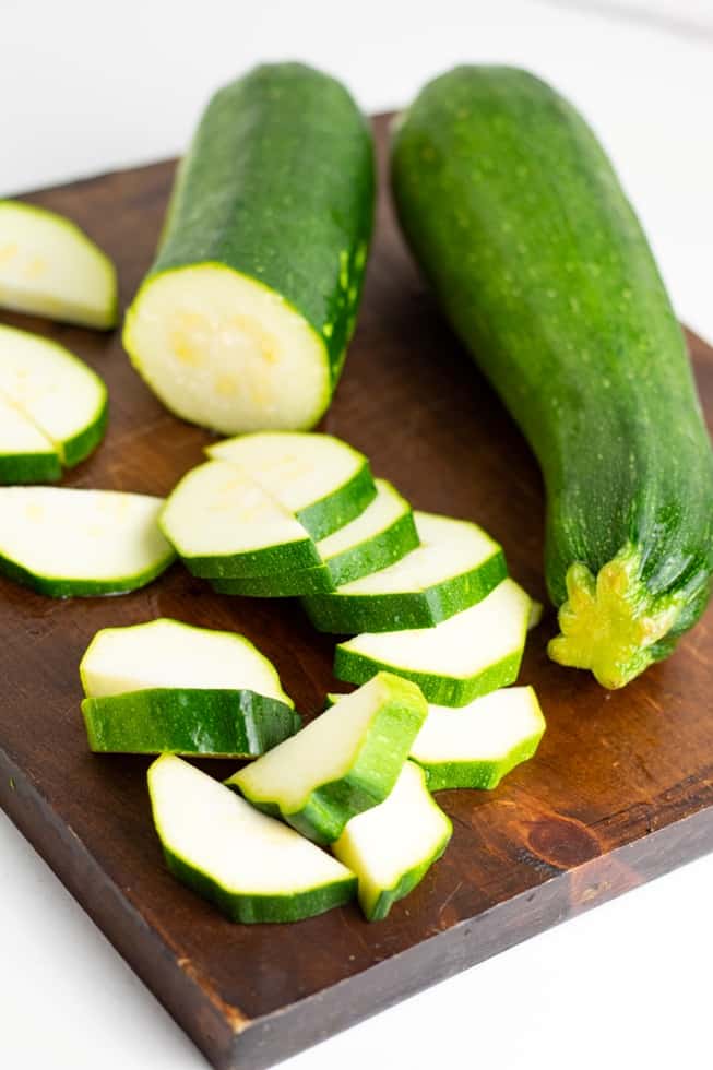 zucchini whole and sliced on dark wood cutting board