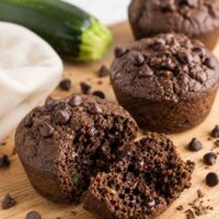 chocolate zucchin i muffins on a wooden board with one open to show moisture and density.