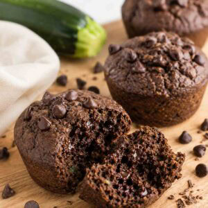 chocolate zucchin i muffins on a wooden board with one open to show moisture and density.