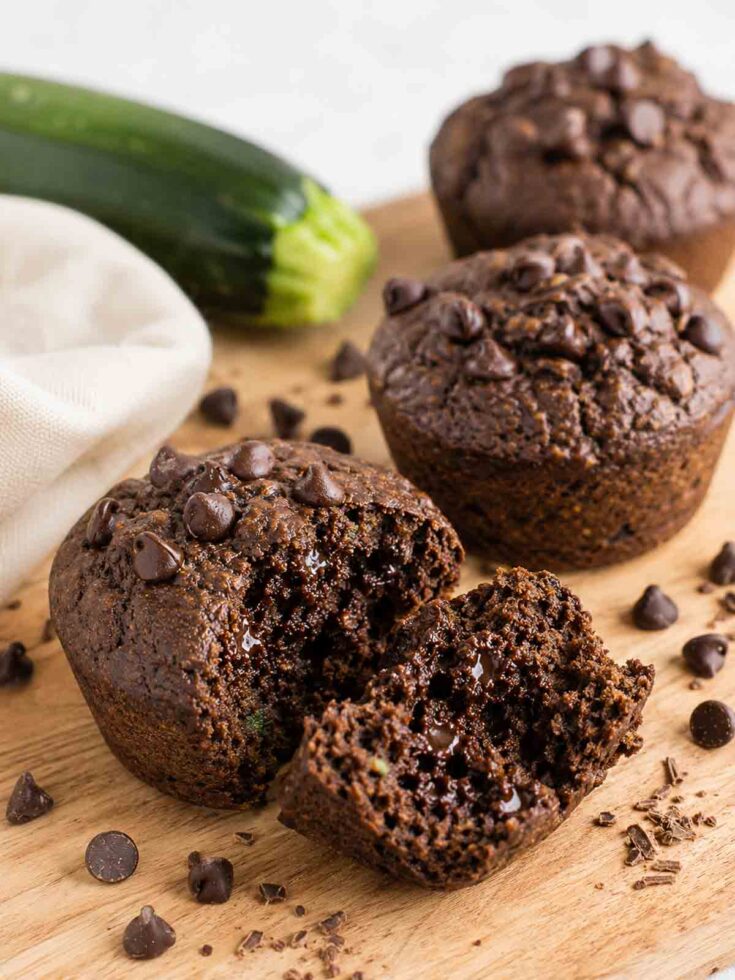 chocolate zucchin i muffins on a wooden board with one open to show moisture and density.