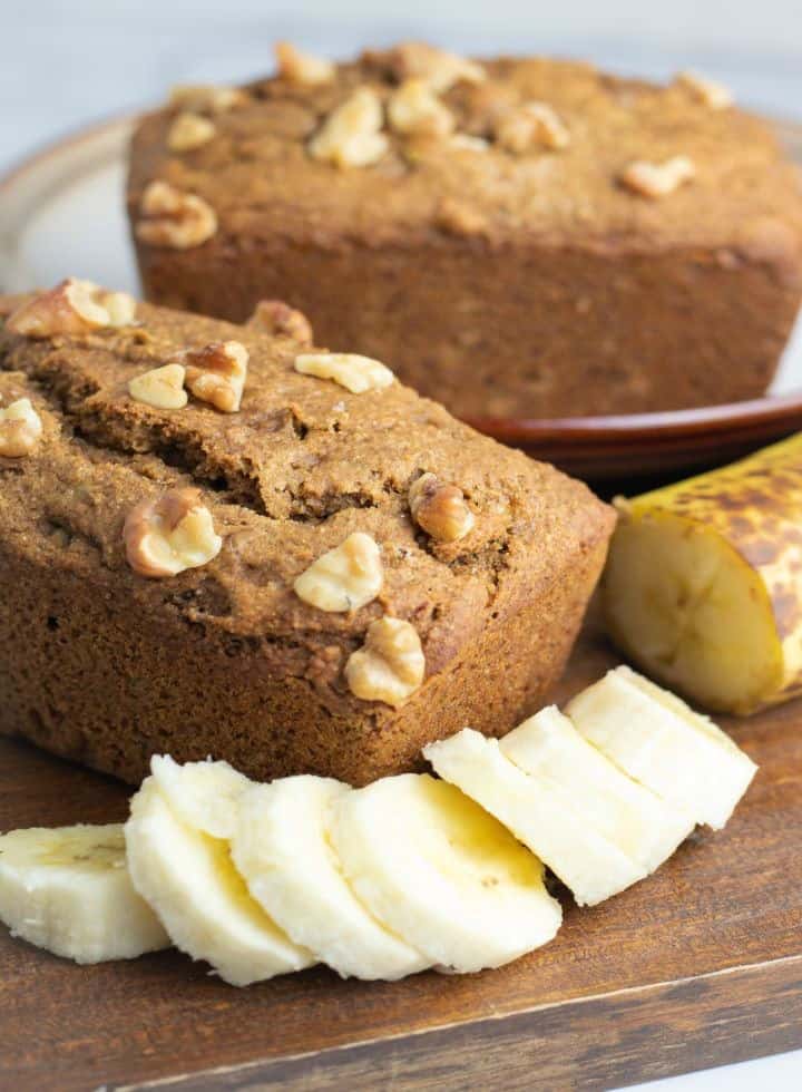 close of of loaf of banana bread with slices of banana in front