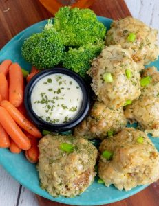 cauliflower buffalo wings stacked on blue plate with white dip broccoli and carrots