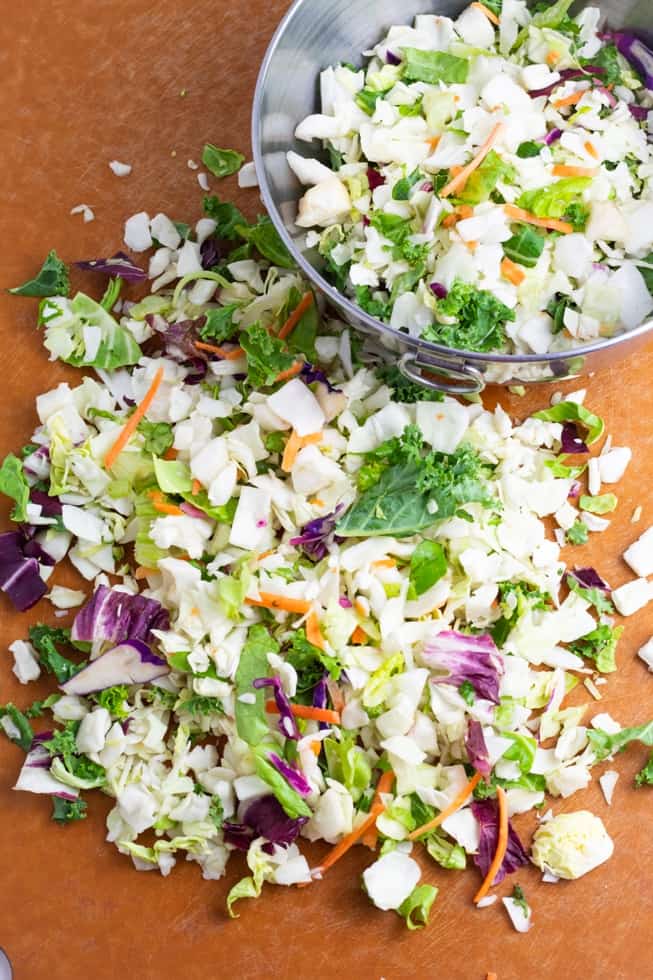overhead shot of chopped coleslaw on cutting board with bowl in background