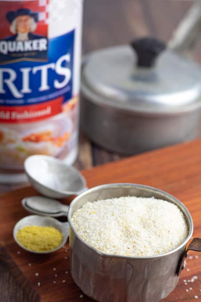 dry uncooked grits in tin measuring cup with quacker package in background
