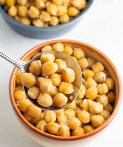 close up of cooked chickpeas in spoon over brown bowl on white background