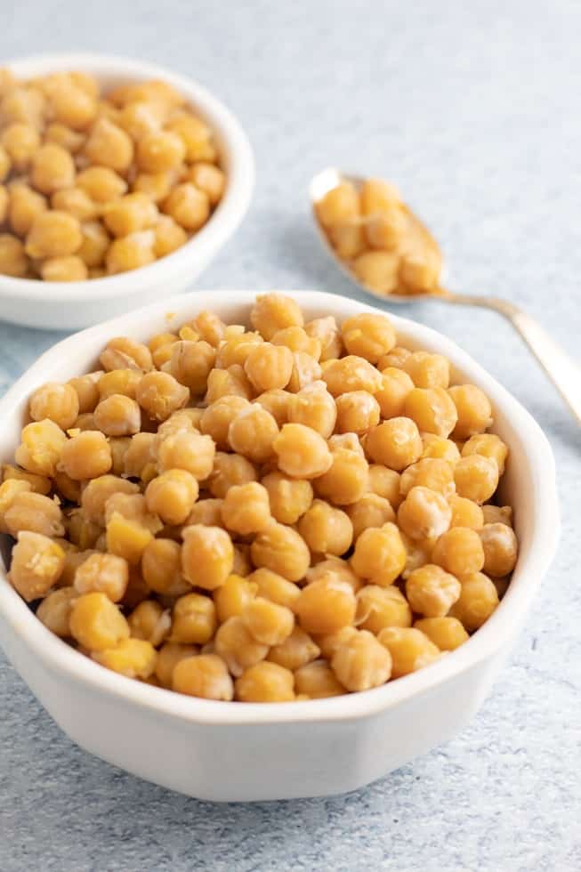 cooked chickpeas in white bowl with spoonful on countertop in background
