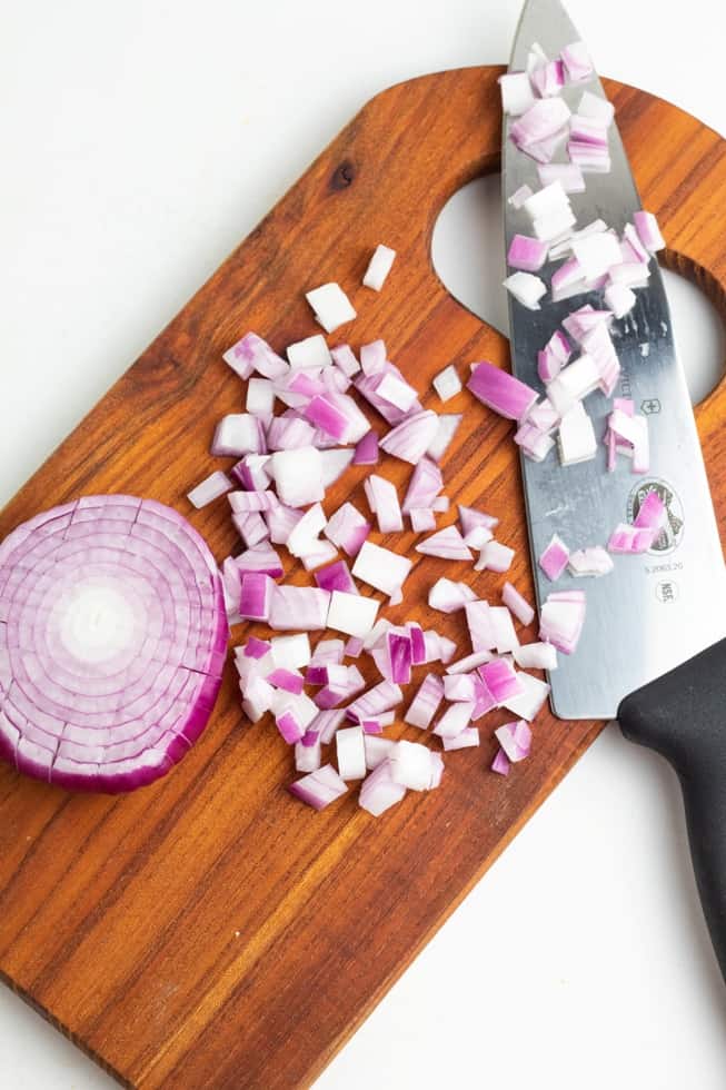 diced red onion on wood cutting board with large chopping knife