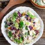 white scalloped bowl filled with vegan coleslaw on rustic wooden table with wooden spoon