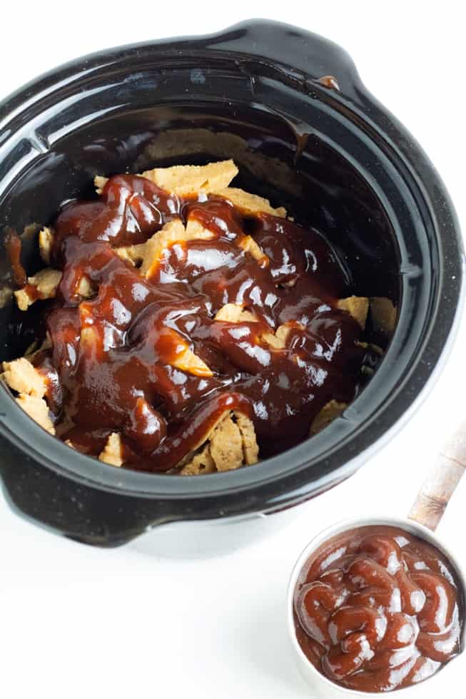 black crockpot full of vegan bbq with tin cup of bbq sauce beside