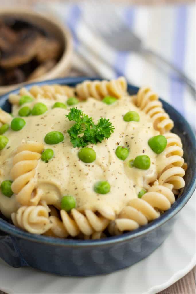 spiral pasta topped with vegan alfredo sauce and green peas in blue round dish