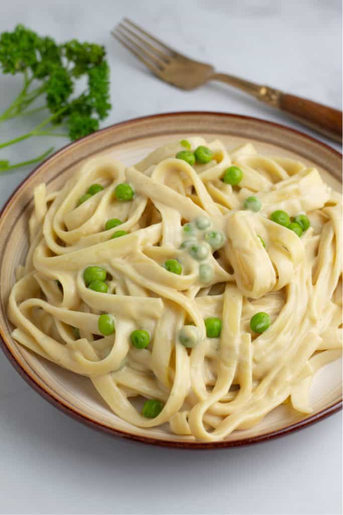 fettuccini noodles topped with vegan alfredo and green peas in brown plate
