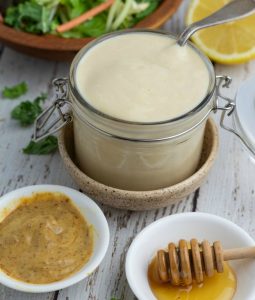 jar filled with honey mustard dressing with small white bowls of dijon mustard and honey setting in front