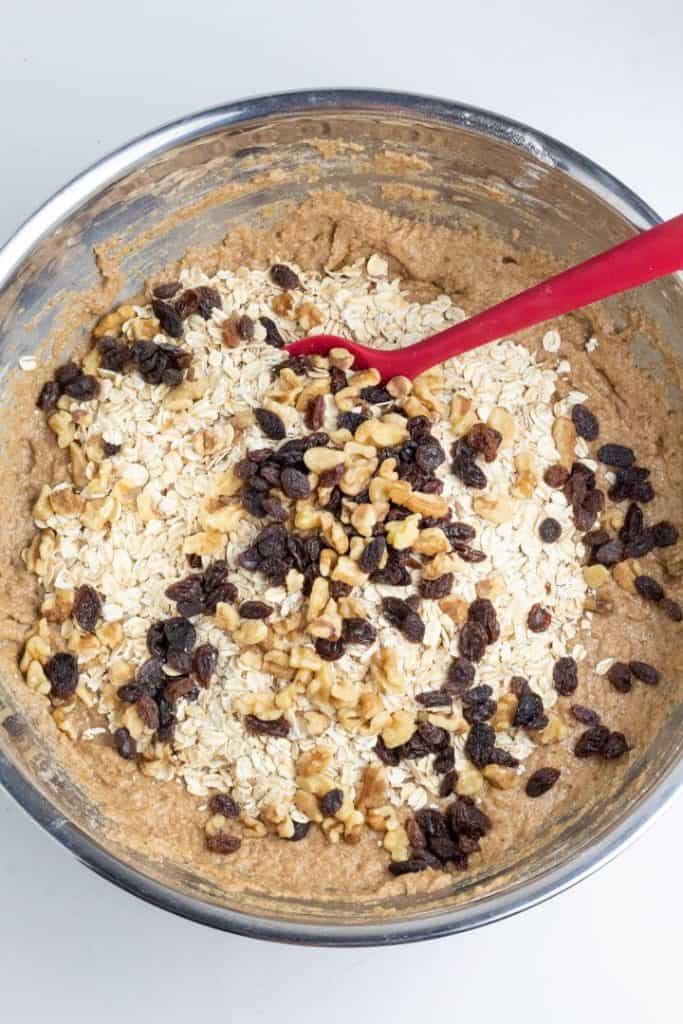 cookie batter with raisins and walnuts in stainless bowl with red spatula