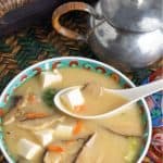 overhead photo of large bowl of miso soup with tofu and mushrooms with white asian soup spoon