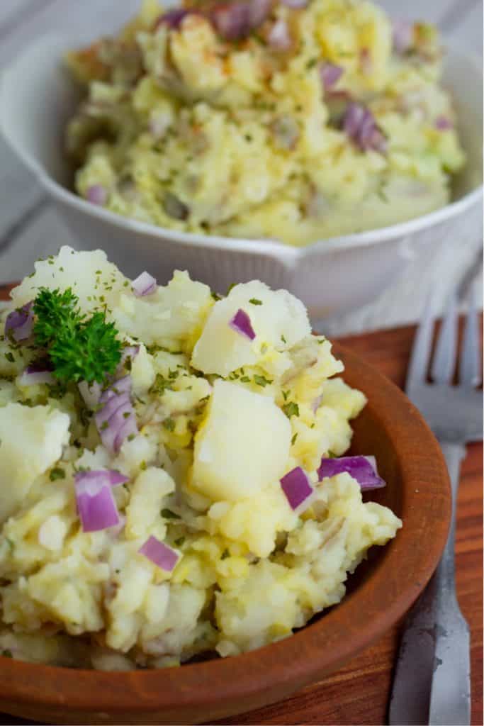 brown wooden bowl with potato salad, white bowl of potato salad in background
