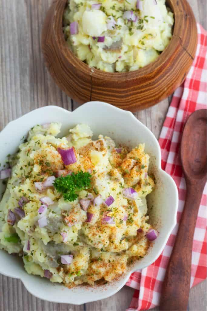 overhead shot of potato salad in white scalloped bowl and wooden bowl with wooden spoon