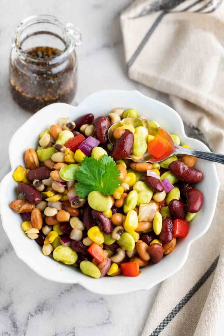 a white bowl of mixed bean salad with dressing beside it.