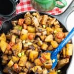 cooked breakfast potatoes in cast iron skillet with bright blue spoon