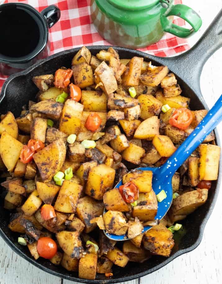 cooked breakfast potatoes in cast iron skillet with bright blue spoon