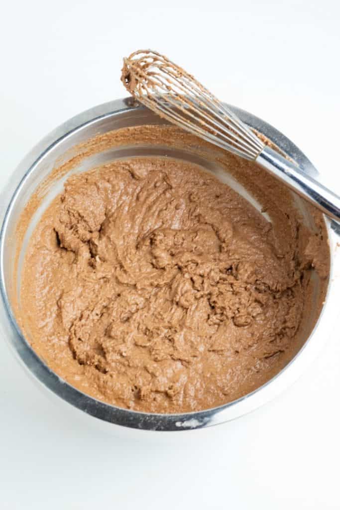 Chocolate cake batter in stainless mixing bowl with whisk