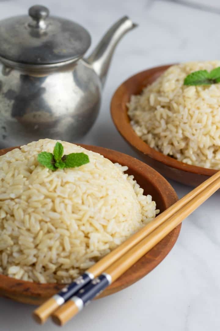 cooked brown rice in wooden bowl with chopsticks teapot in background