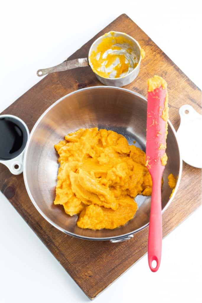 stainless bowl with mashed pumpkin on cutting board with measuring cups