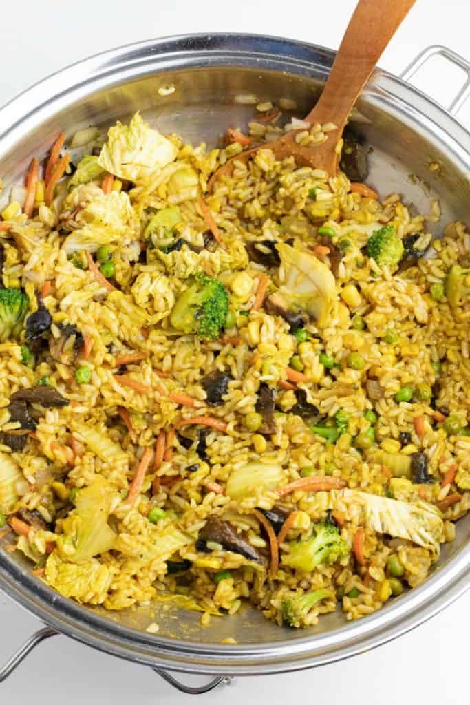 stainless wok full of vegan fried rice with wooden spoon stirring