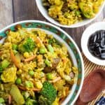 overhead shot of bowls filled with vegan fried rice with wooden spoon and brown sauce