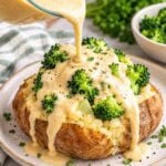cashew alfredo being poured over a baked potato with broccoli florets.