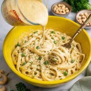 cashew alfredo being poured into a bowl of pasta.