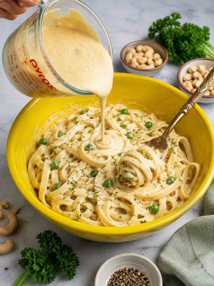 cashew alfredo being poured into a bowl of pasta.