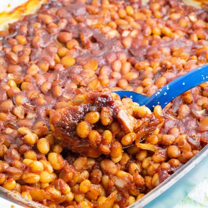 casserole dish full of vegan baked beans being scooped out with bright blue spoon