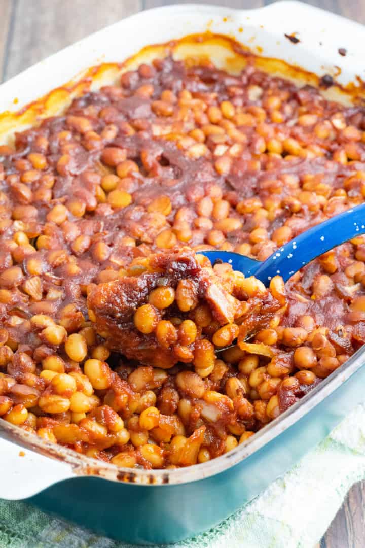 casserole dish full of vegan baked beans being scooped out with bright blue spoon
