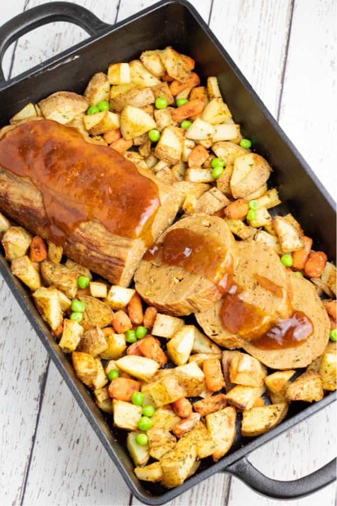 overhead shot of vegan roast with roasted potatoes and carrots in cast iron baking dish