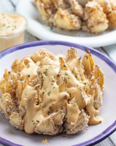 vegan blooming onion on plat with blue rim covered in chipotle sauce