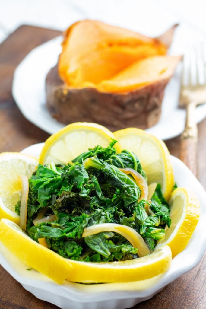 cooked kale in white bowl with lemon slices