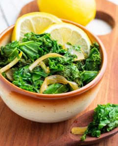 braised kale in brown and white bowl with lemon slices
