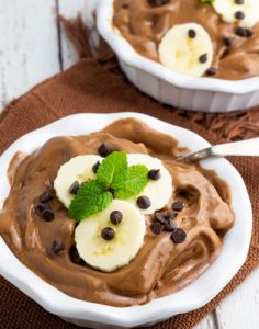 two white bowls with chocolate banana nice cream topped with sliced bananas, dairy free chocolate chips, and mint leaves