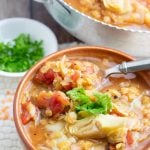 brown bowl of lentil stew with artichokes and spoon