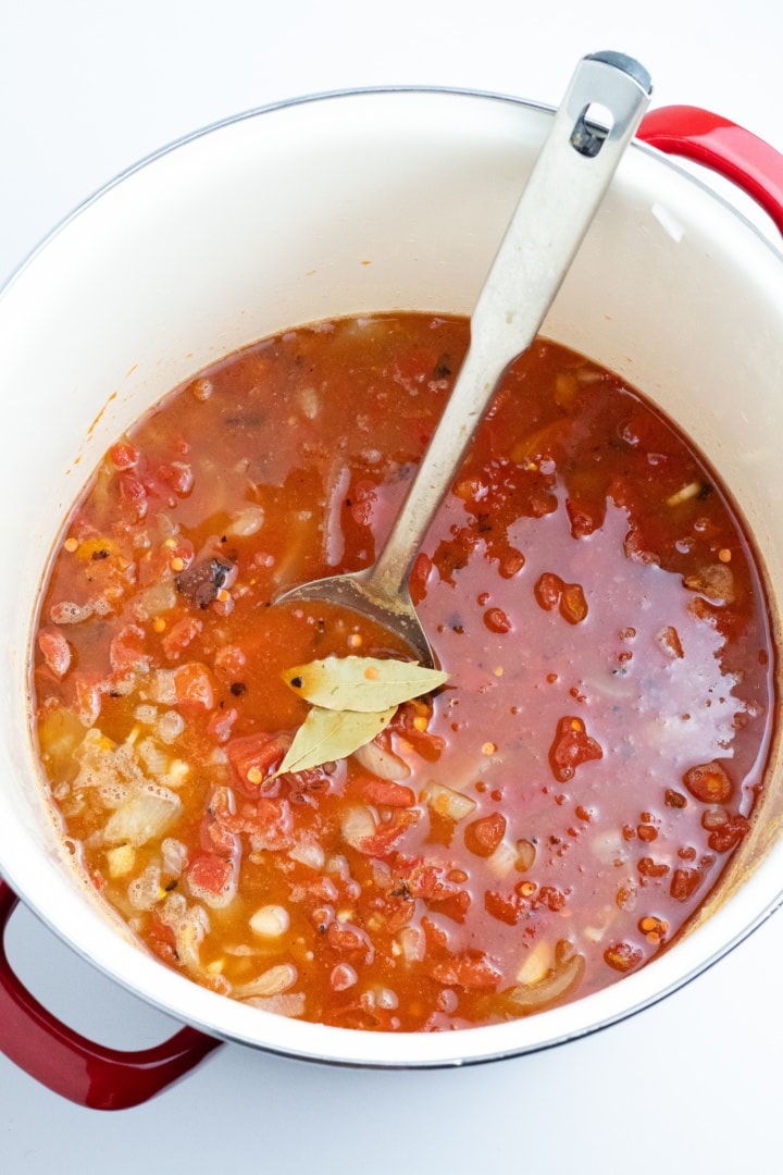 large stockpot full of lentil soup topped with bay leaves and spoon